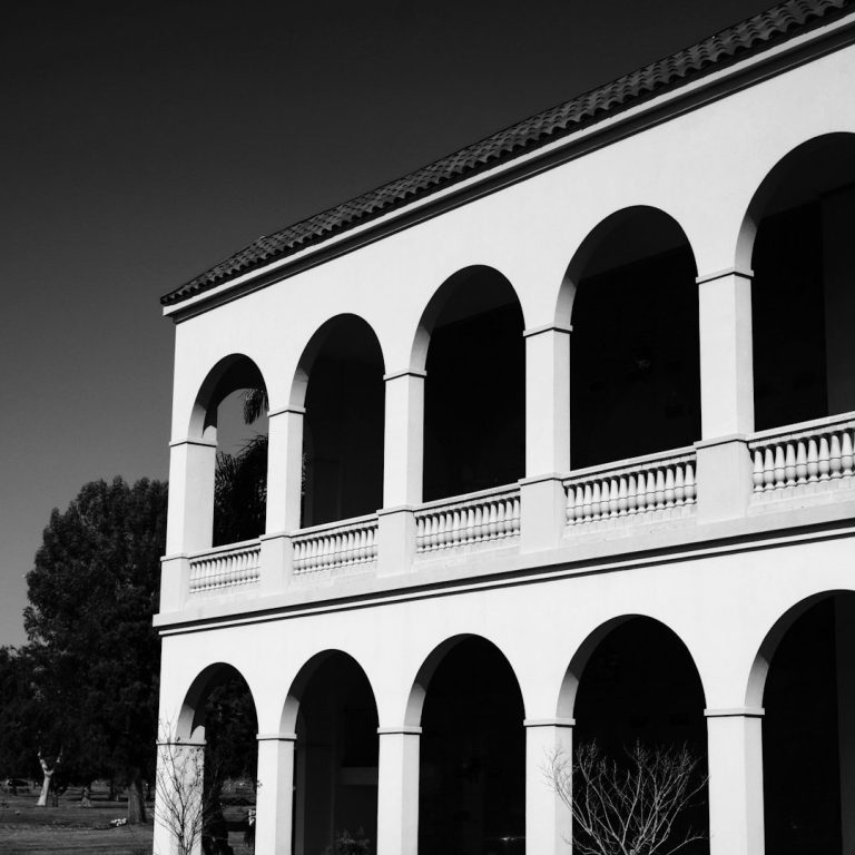 Weißes Gebäude mit Bögen, baumumsäumt und im Hintergrund eine Landschaft.
Fassadenreinigung