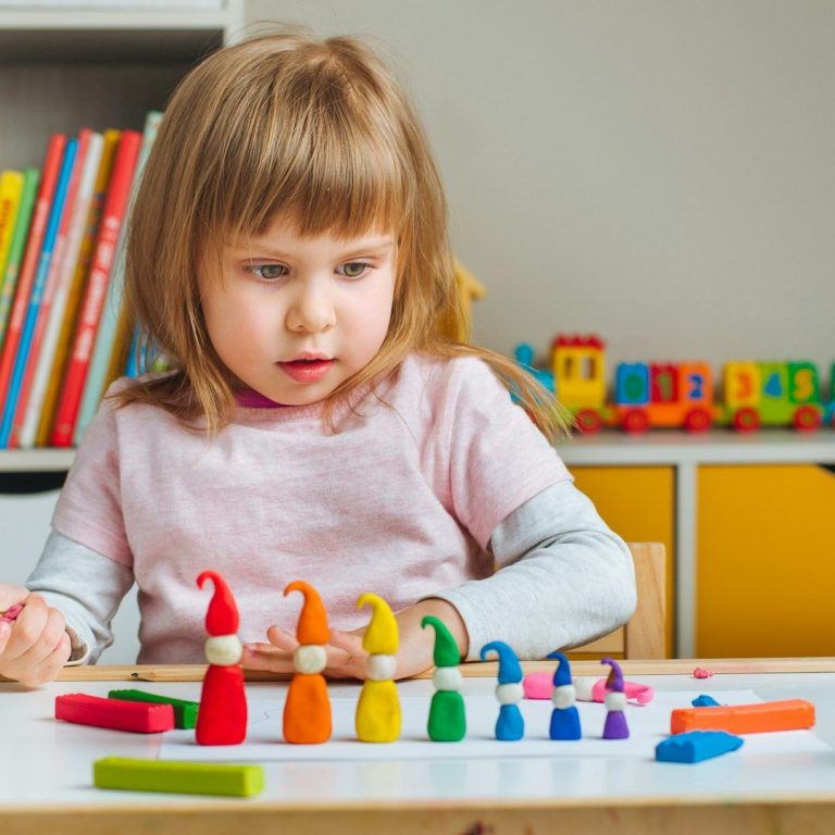 Ein kleines Mädchen spielt mit buntem Knete und formt Figuren auf einem Tisch.